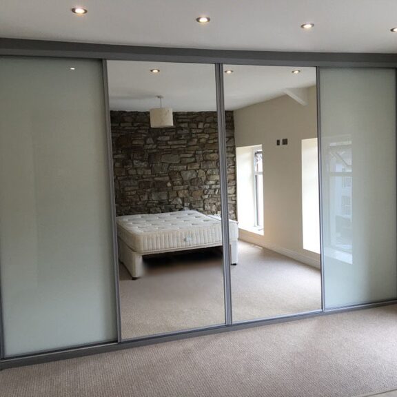 Mirror and frosted panel sliding wardrobe doors reflecting a stone wall in Taffs Well