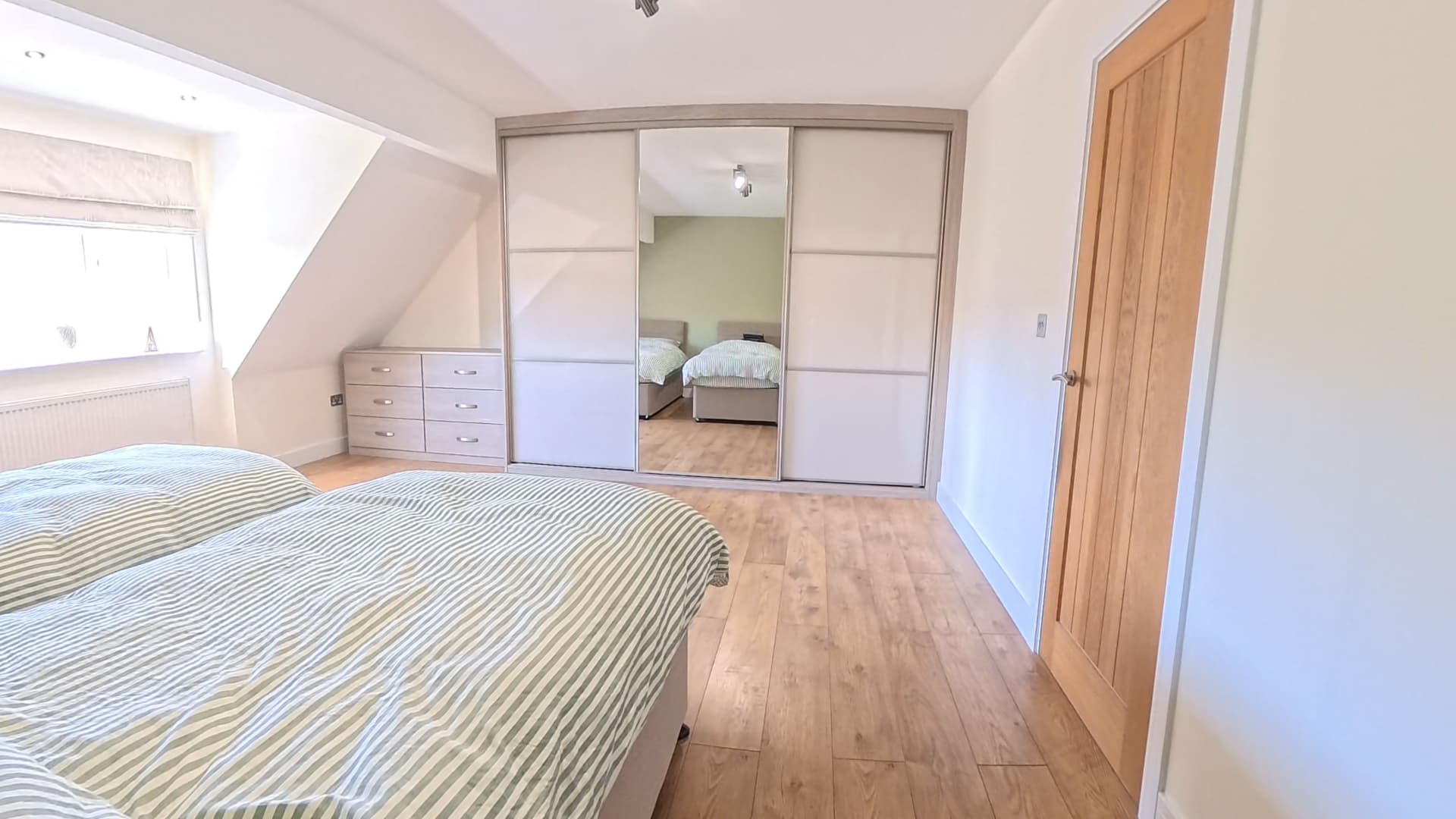 The same bedroom fitted with panel and mirror sliding wardrobe doors beneath the sloping ceiling