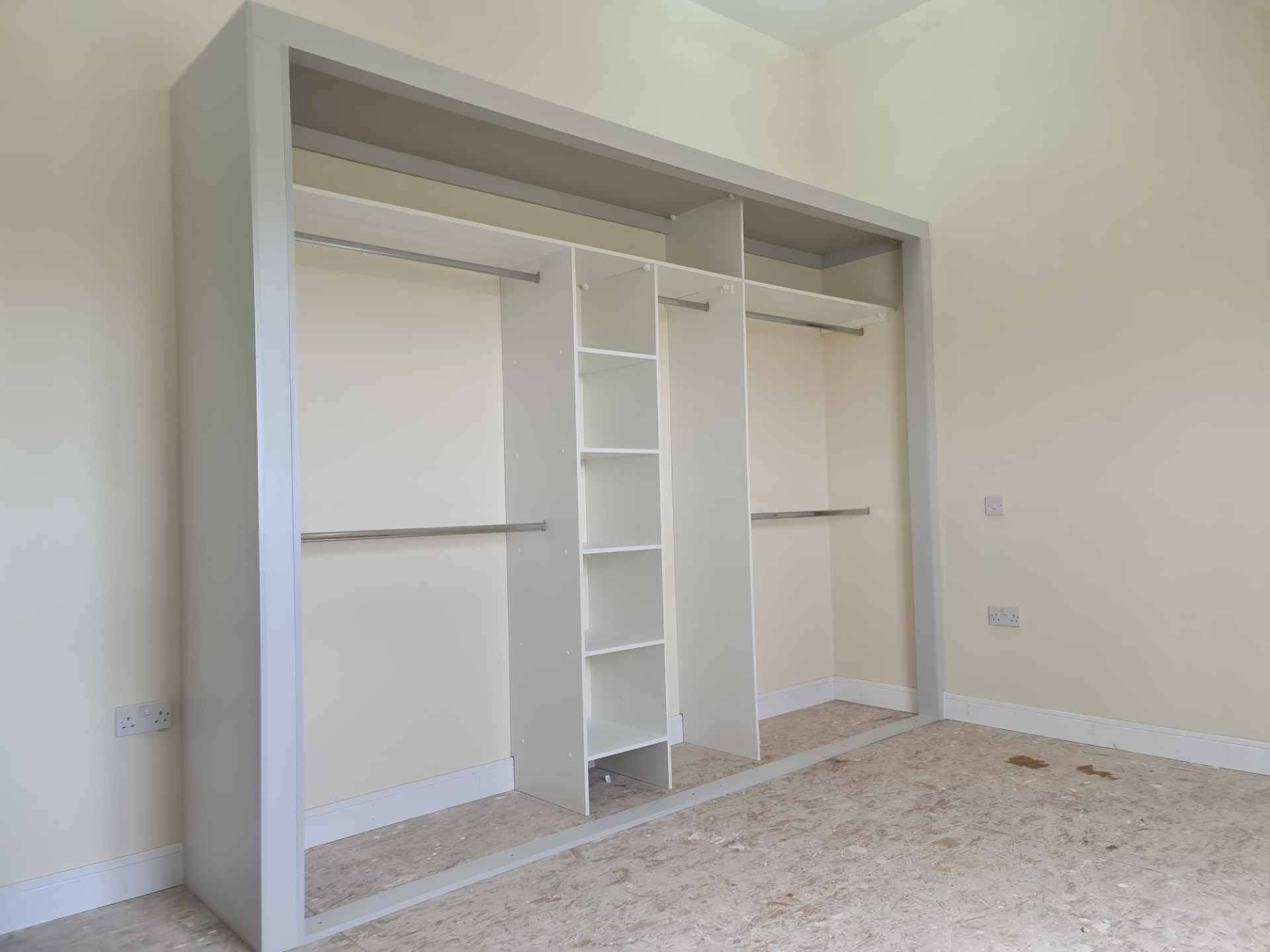 Light fitted wardrobe interior with hanging rails and open shelves in a Treforest bedroom