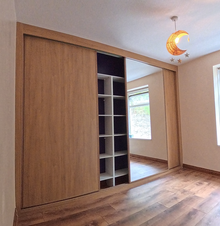 Oak effect solid panel sliding wardrobe doors slid open to show white interior shelving in a Ystrad Mynach bedroom