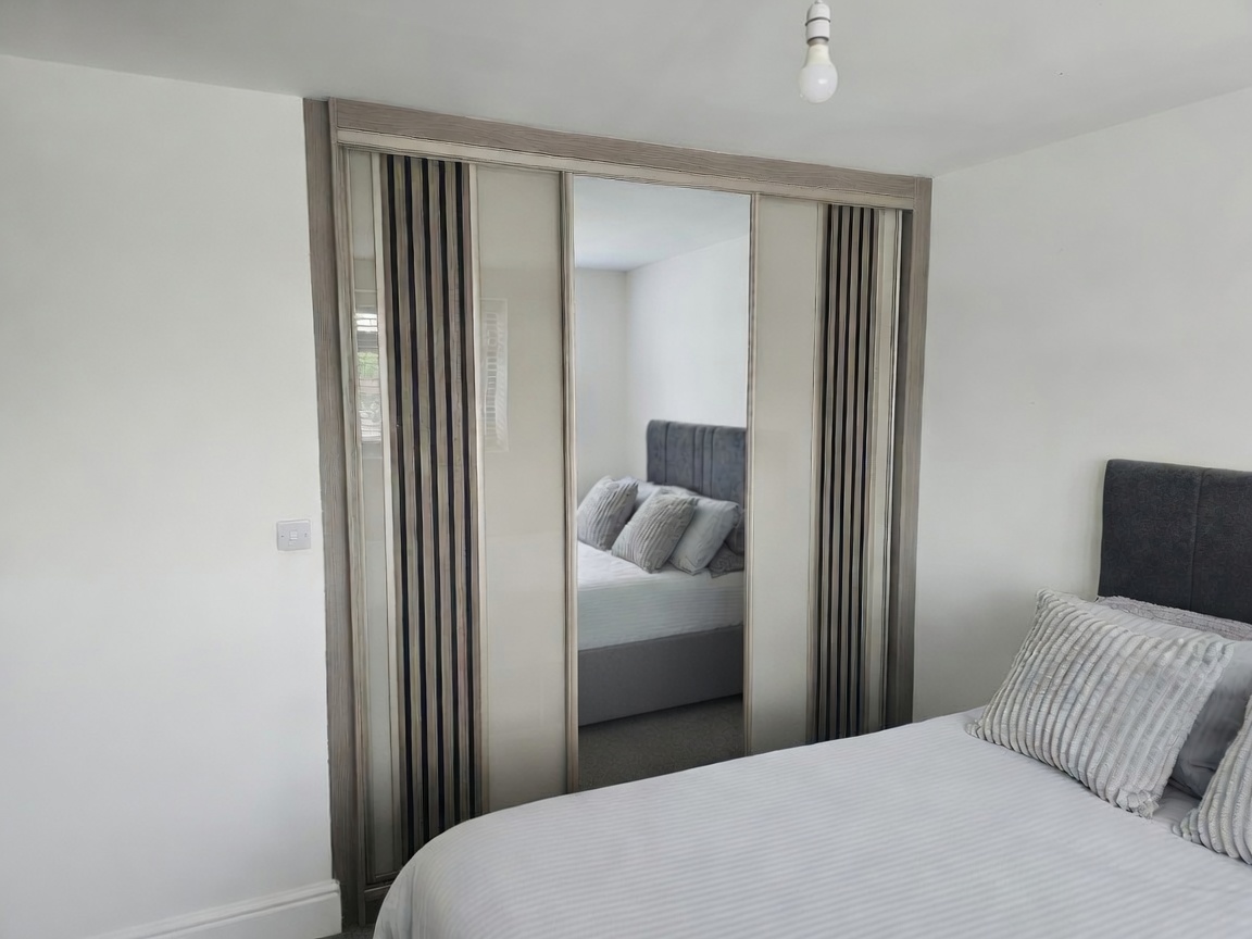 Acoustic-style panel sliding wardrobe doors with a central mirror in a Swansea bedroom