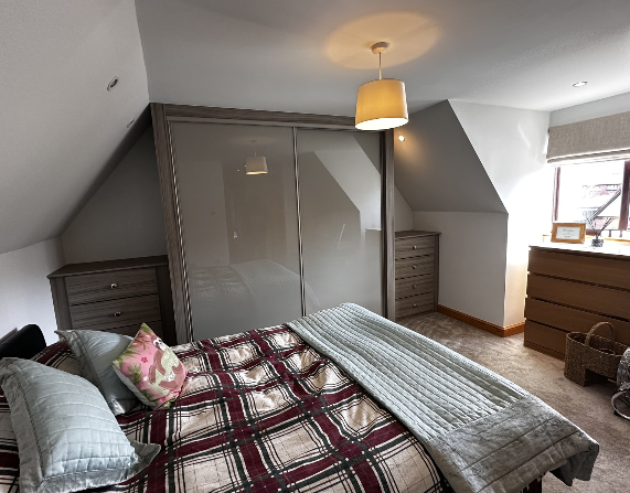 The same loft bedroom fitted with grey sliding wardrobe doors beneath the sloping ceiling