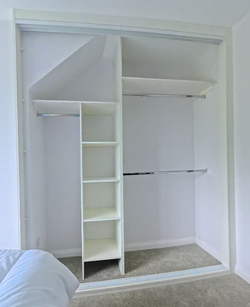 The same alcove fitted with white shelves, hanging rails and storage compartments behind sliding doors