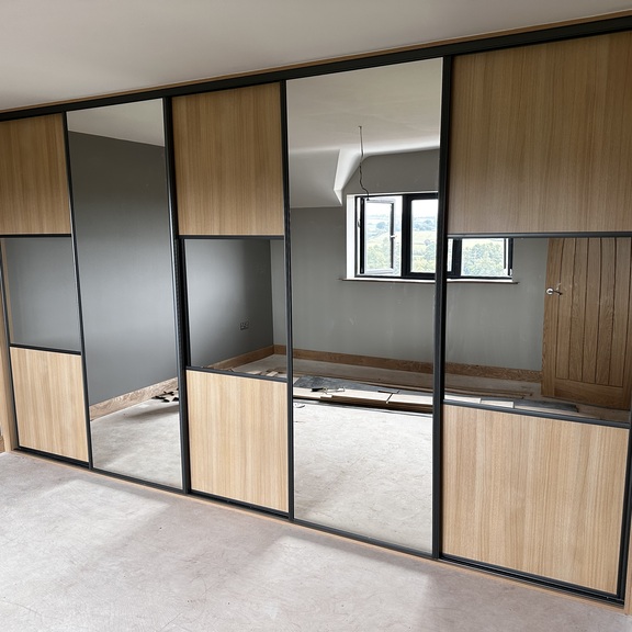 Oak effect solid panel sliding wardrobe doors with mirror and dark grey inserts in a Cardiff bedroom