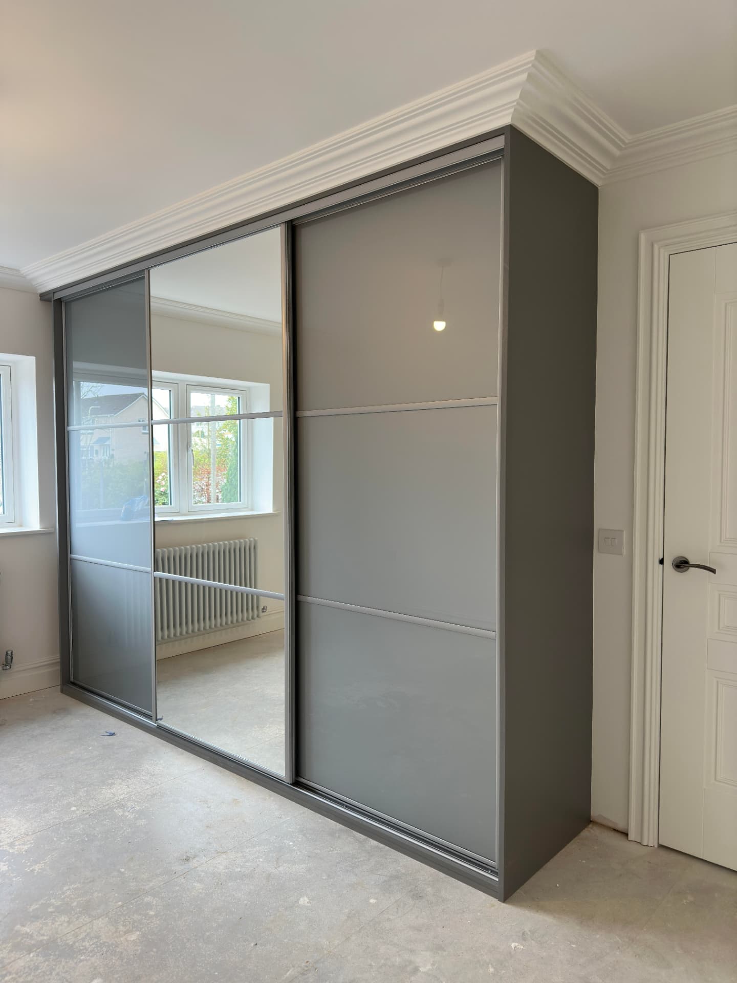 Grey solid panel sliding wardrobe doors with a central mirror section in a Beddau bedroom